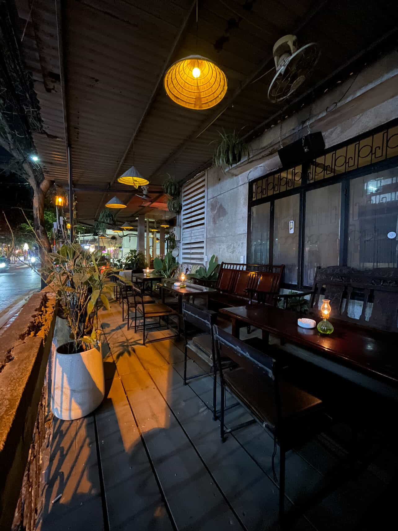Street-side terrace at night with conical pendant lamps and oil-lamp candles on the tables